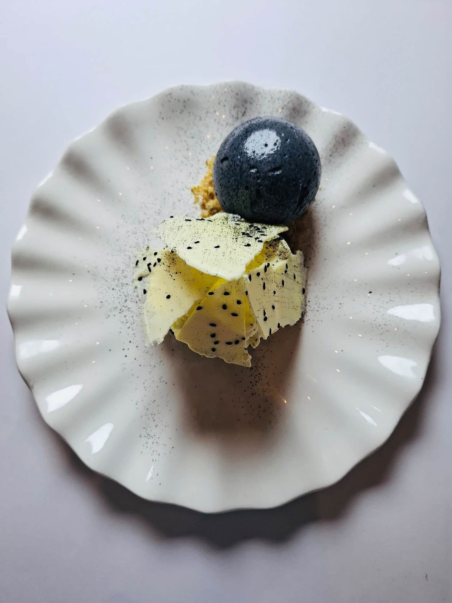Black sphere dessert with white chocolate on a fluted white plate