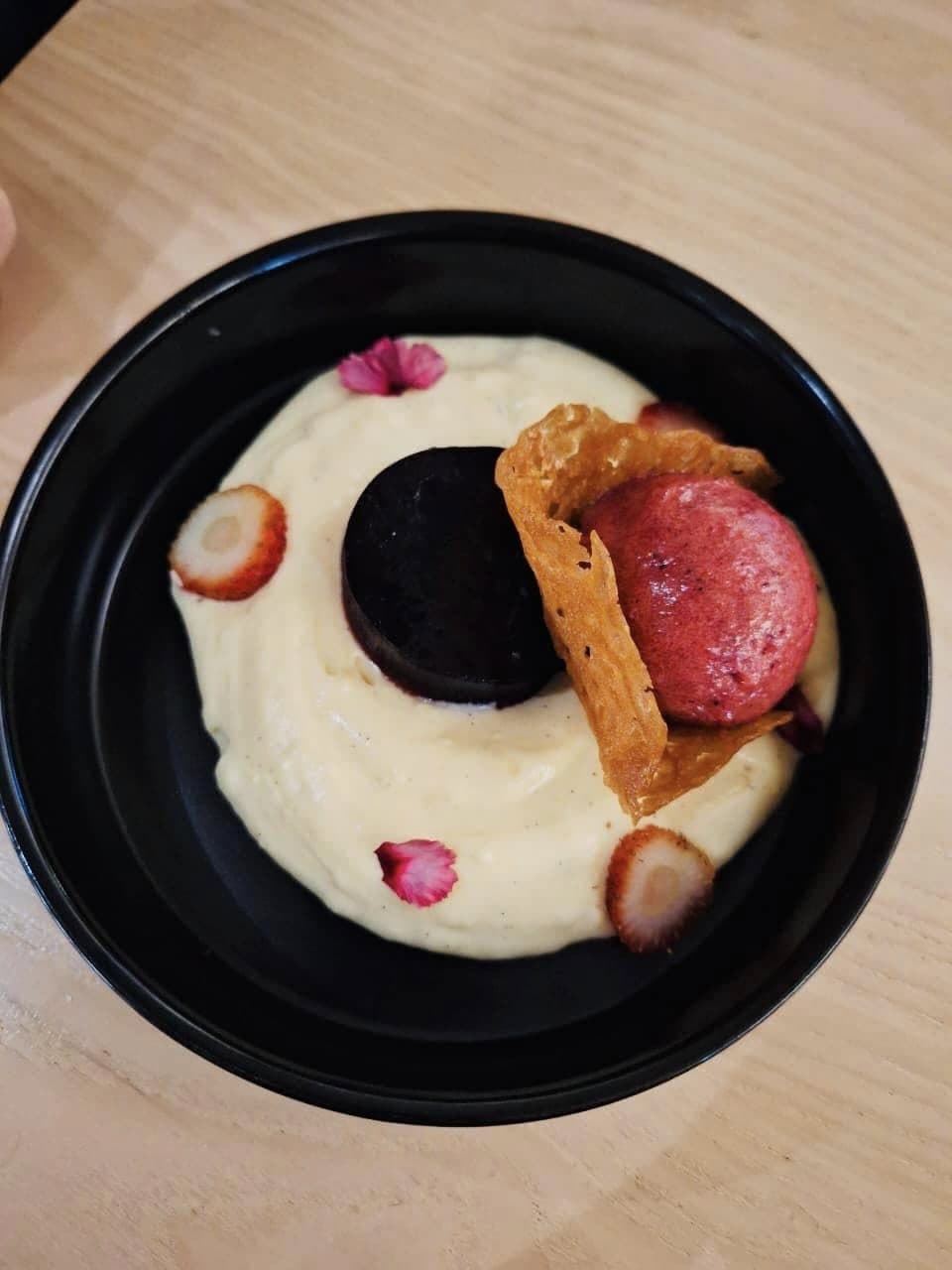 Chocolate dessert with berry sorbet, crisp tuile and cream in a dark bowl
