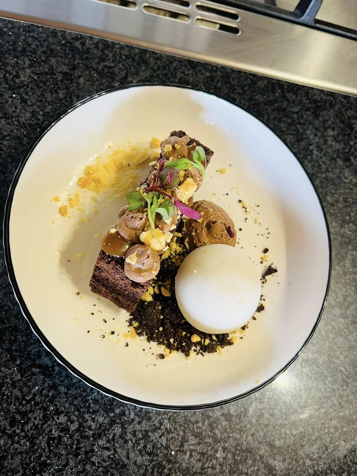 Chocolate dessert with a white sphere, crumb and edible flowers