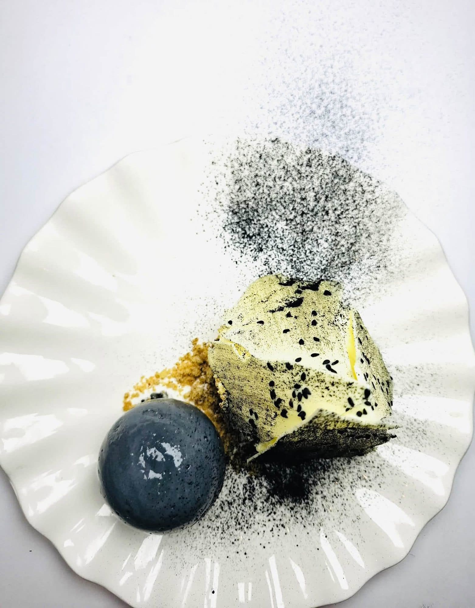 Gold-dusted dessert with a black sphere on a fluted white plate