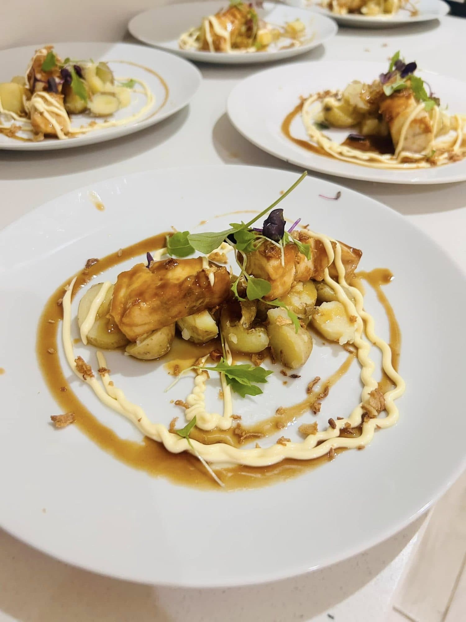 Pan-fried dumplings on a white plate with a glossy jus and fresh herbs