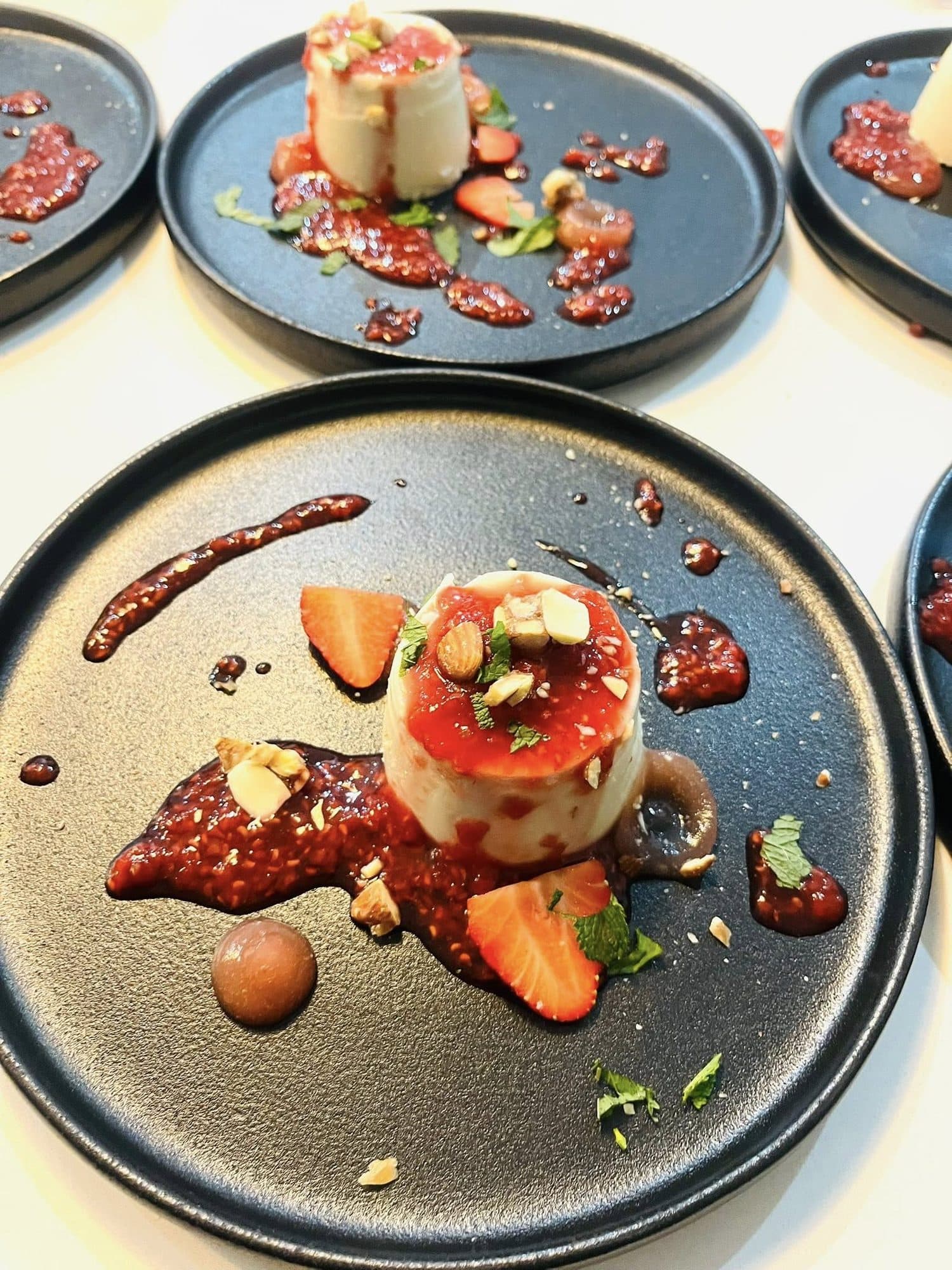 Set cream dessert with fresh strawberries and berry coulis on a dark plate