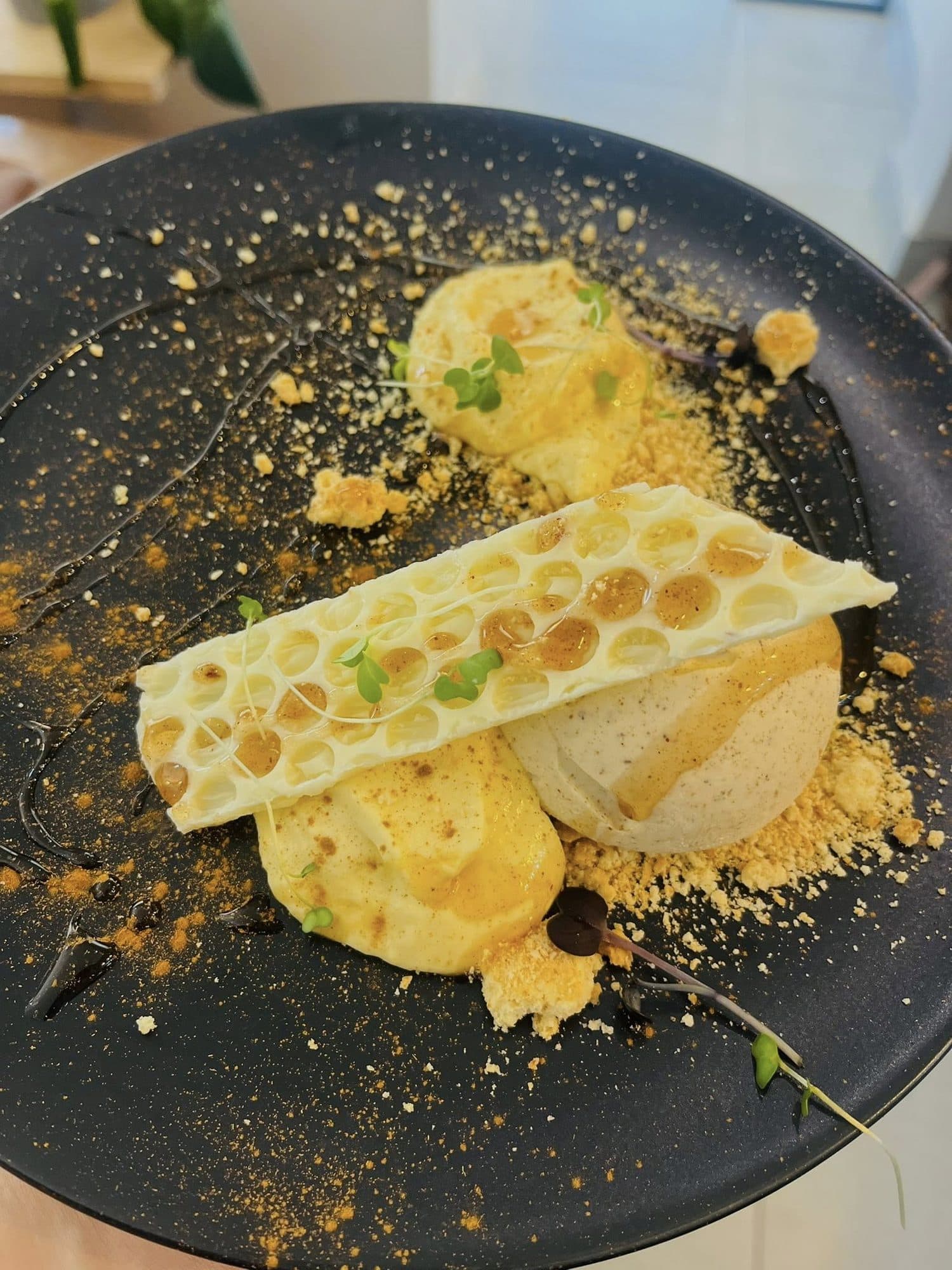 Plated dessert with a honeycomb tuile, sabayon and golden crumb on a dark plate