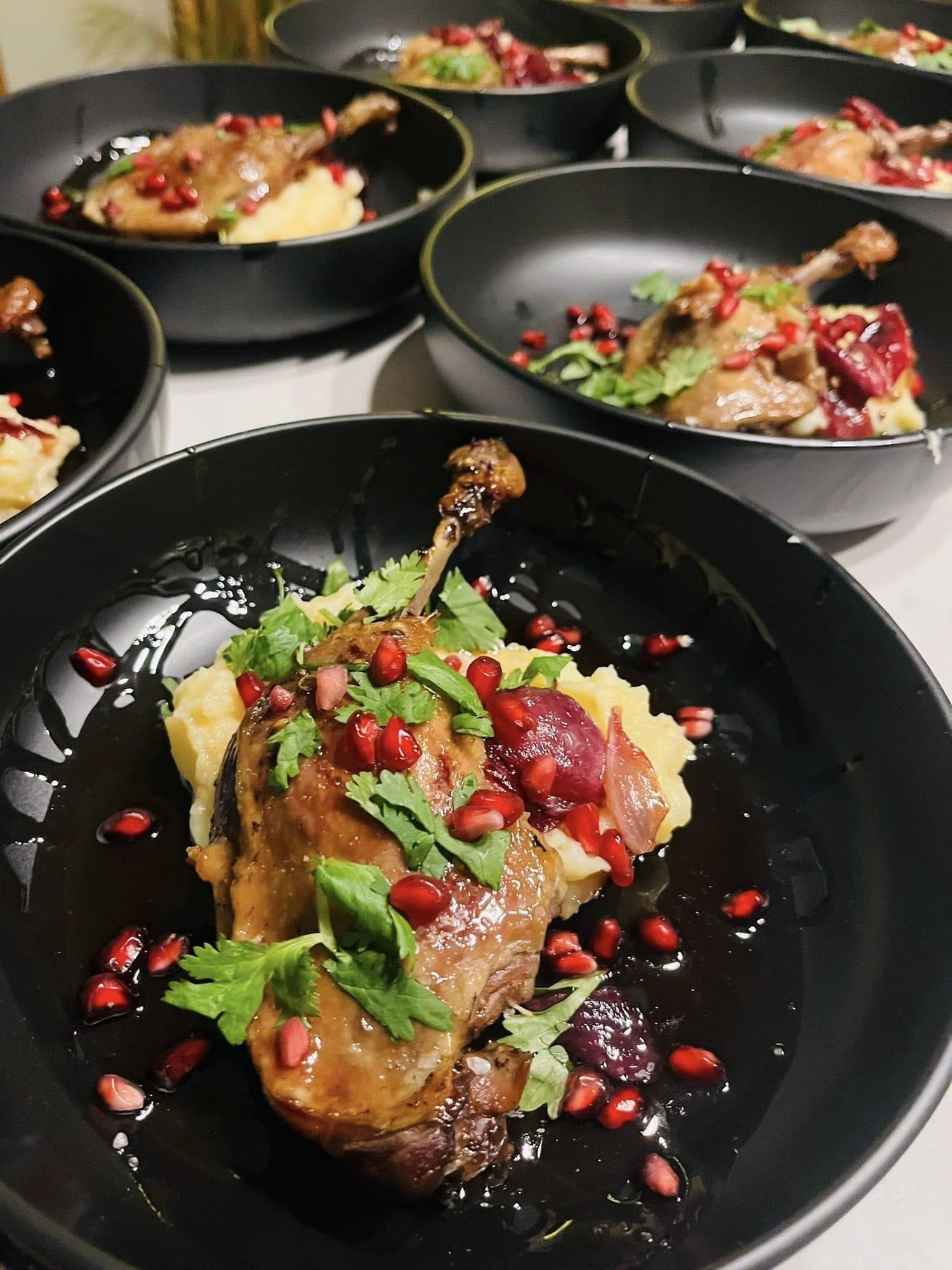 Roasted leg served in a dark bowl with pomegranate jewels and herbs