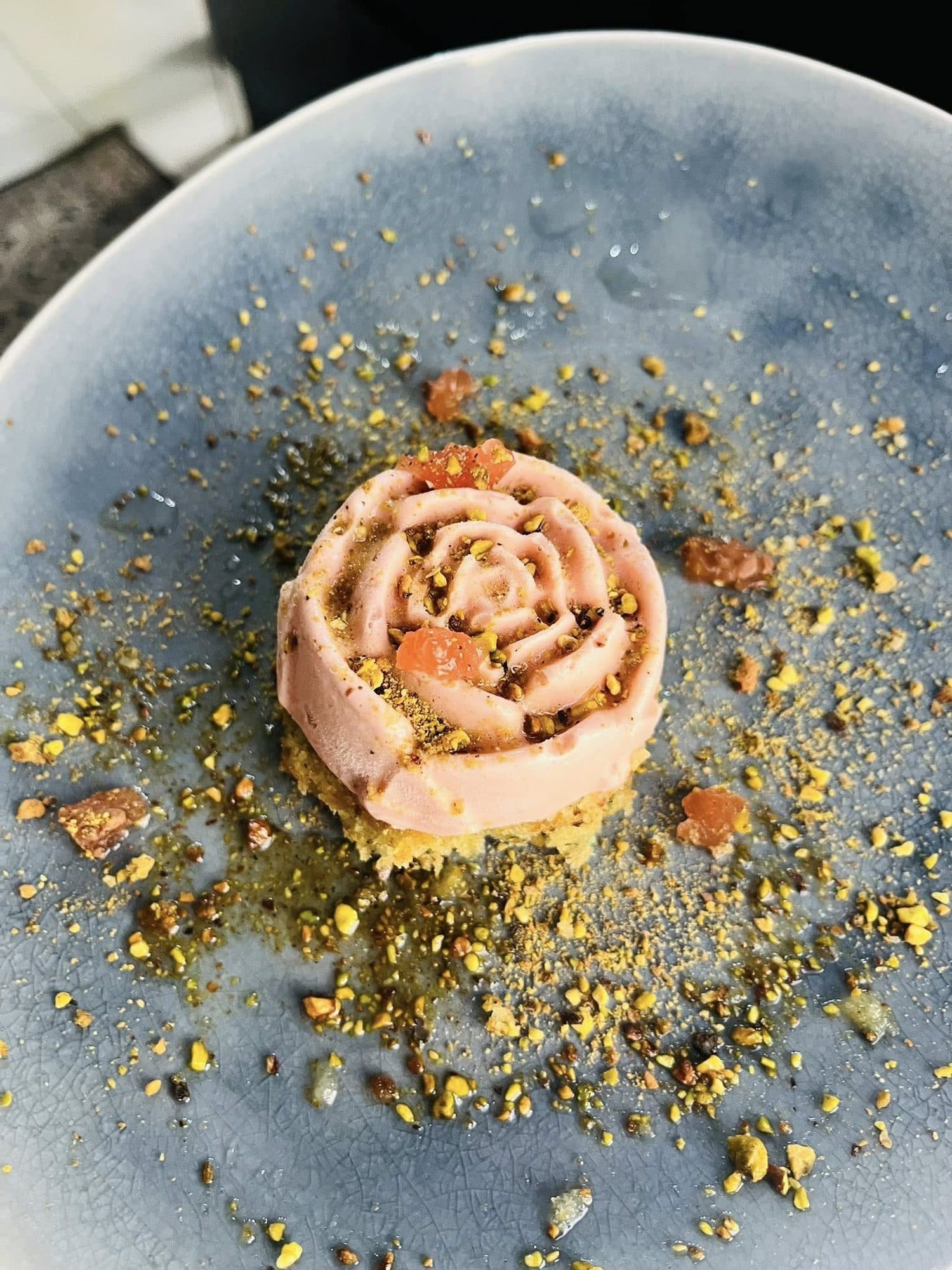 Rose mousse finished with pistachio crumb on a speckled plate