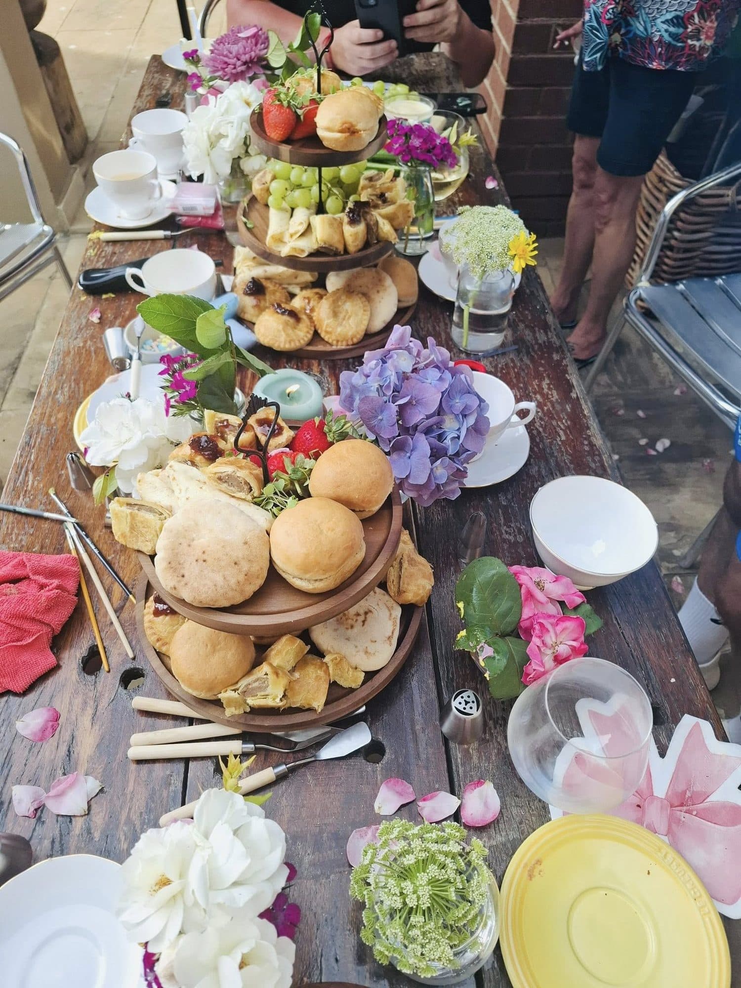 Tiered high-tea stands with pastries and fresh flowers on a long table