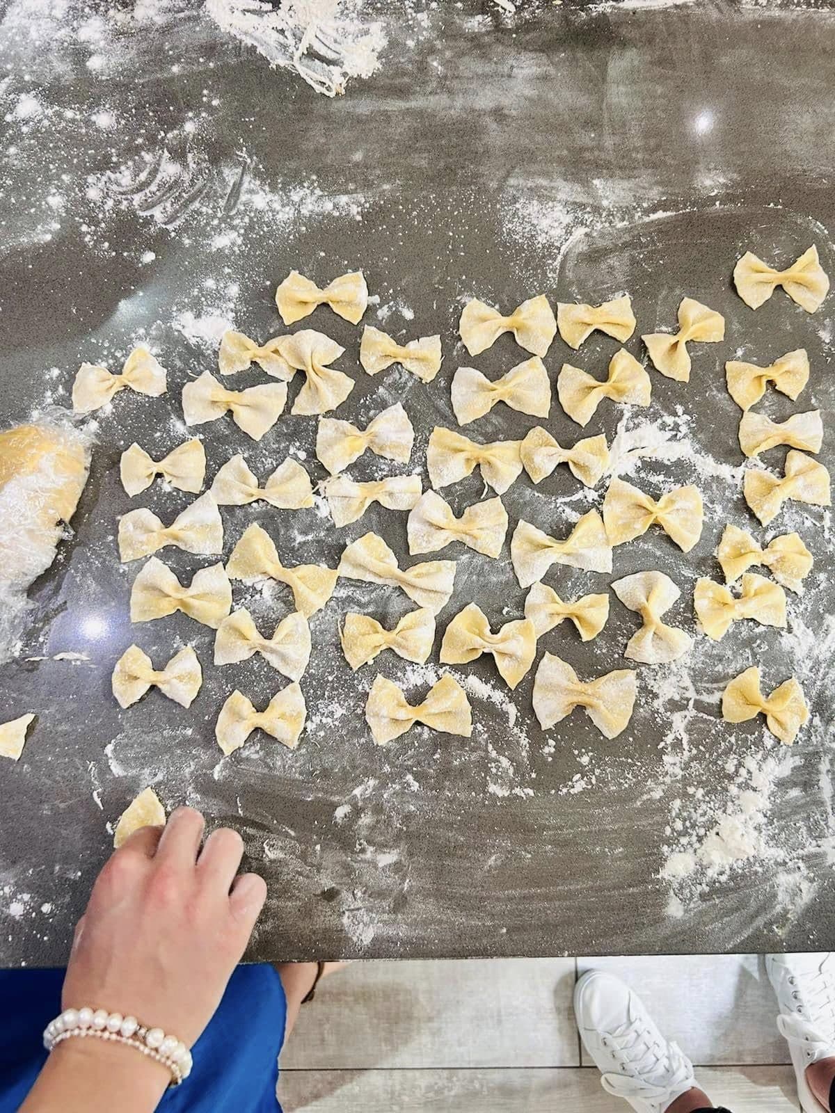 Fresh farfalle being shaped by hand on a floured table